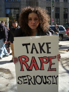 A woman holding a sign, "Take Rape Seriously"