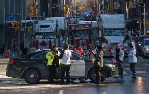 A police car in front of three columns of trucks occupying a street in downtown Ottawa, Ontario.
